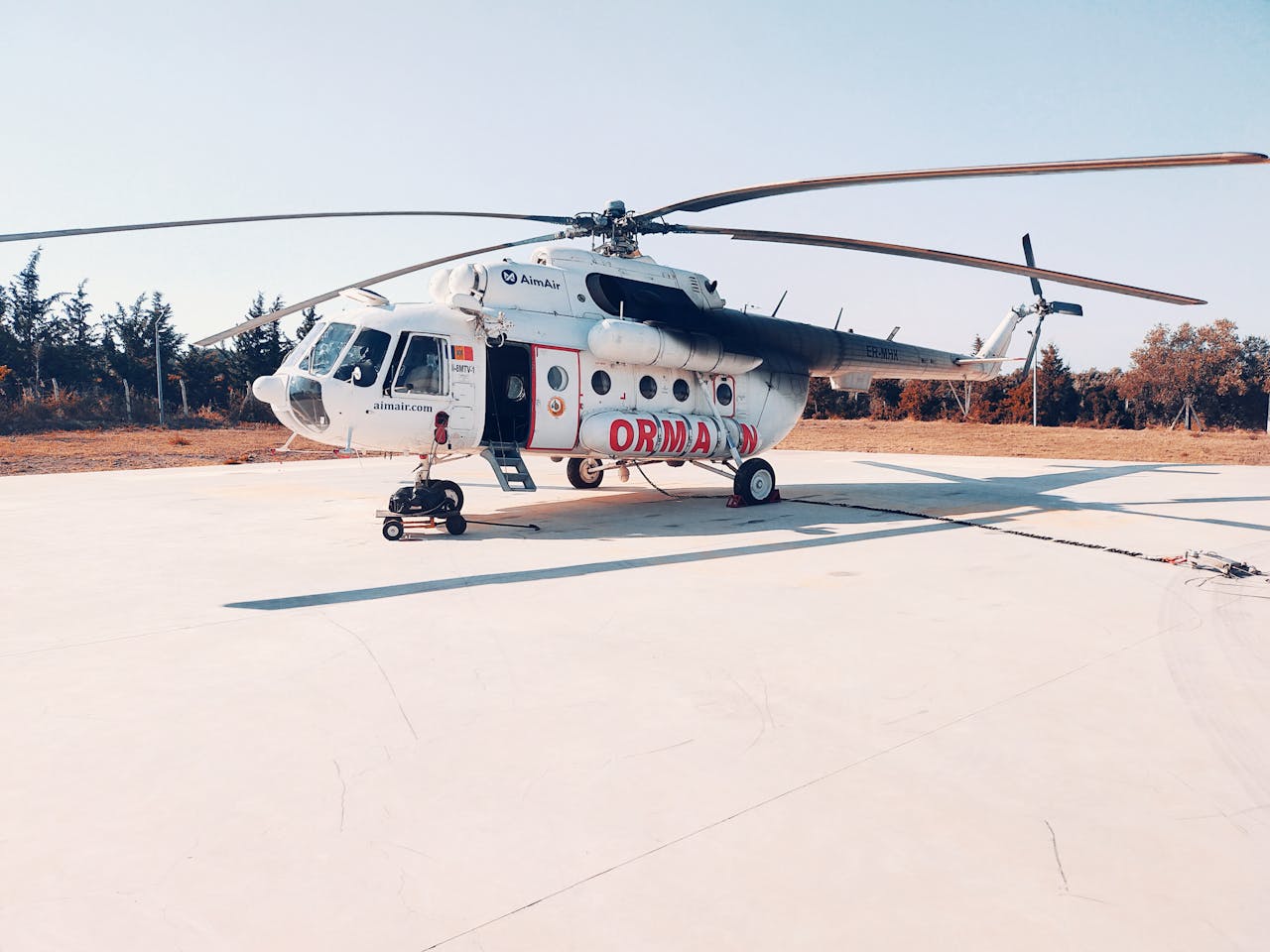 why-choose-us White helicopter parked on a tarmac under a clear blue sky.